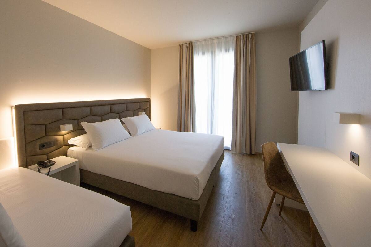 A hotel room with a large bed, a smaller bed, a desk, and a TV mounted on the wall.