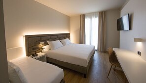 Habitación de hotel con una cama grande, una cama más pequeña, un escritorio y un televisor montado en la pared.