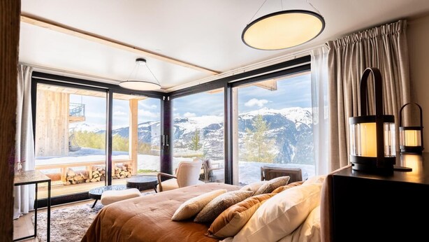 A modern hotel room with a large bed, a desk, and a view of snow-capped mountains. - Chalet, 100m from ski slopes, Ground floor, view mountain, sauna, terrace, balcony (La Plagne)