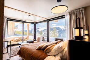 Ein modernes Hotelzimmer mit einem großen Bett, einem Schreibtisch und Blick auf schneebedeckte Berge.