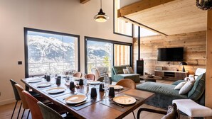 A dining area with a mountain view, wooden walls, and a cozy seating area with a TV. - Chalet, 100m from ski slopes, Ground floor, view mountain, sauna, terrace, balcony (La Plagne)