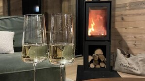 Two empty wine glasses on a wooden table in a modern living room with a large window and a wood-burning stove in the background. - Chalet, 100m from ski slopes, Ground floor, view mountain, sauna, terrace, balcony (La Plagne)