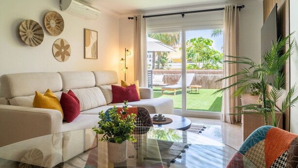 Una sala de estar con un sofá, una mesa de centro y vistas a un patio trasero con terraza y vegetación.