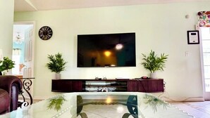 A living room with a flat-screen TV mounted on the wall, a glass coffee table, and two potted plants. - Ref 902. Stunning villa own pool, games room. Near Disney (Four Corners)