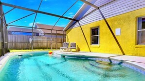A swimming pool with a covered area, a yellow wall, and two chairs.