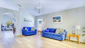 A spacious living room with two blue sofas, a wooden coffee table, and a modern chandelier.