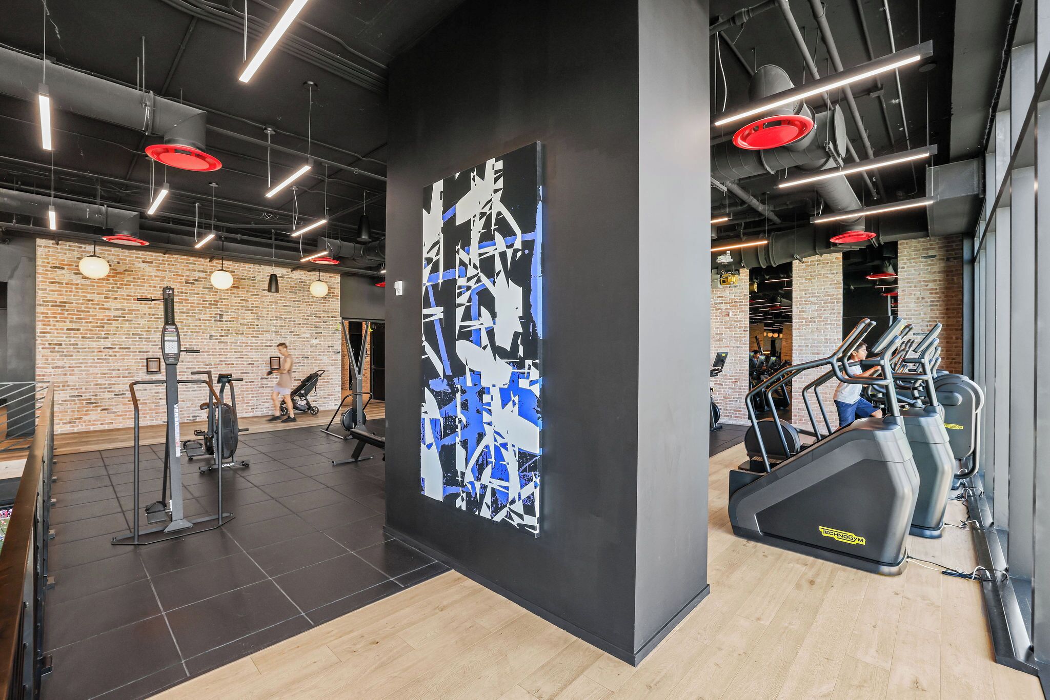 Une salle de sport équipée de matériel d’exercice, un grand tableau abstrait et un mur en briques.