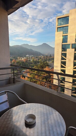 A balcony with a table and chairs, overlooking a cityscape with mountains and buildings. - Lyon Suite (Santiago)