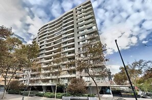 A multi-story residential building with balconies, surrounded by trees and a clear sky. - Lyon Suite (Santiago)