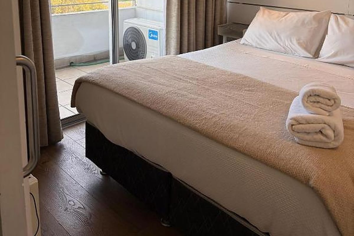 A hotel room with a large bed, a view of the city, and an air conditioning unit.