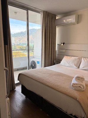 A hotel room with a large bed, a view of the city, and an air conditioning unit. - Lyon Suite (Santiago)
