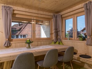 Puupaneloitu huone, jossa on pitkä pöytä, neljä tuolia ja suuret ikkunat, joissa on verhot.