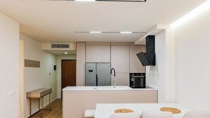 A modern kitchen with a central island, built-in appliances, and a dining area with a marble table and chairs. - Adam & Eve Apartment (Sarande)