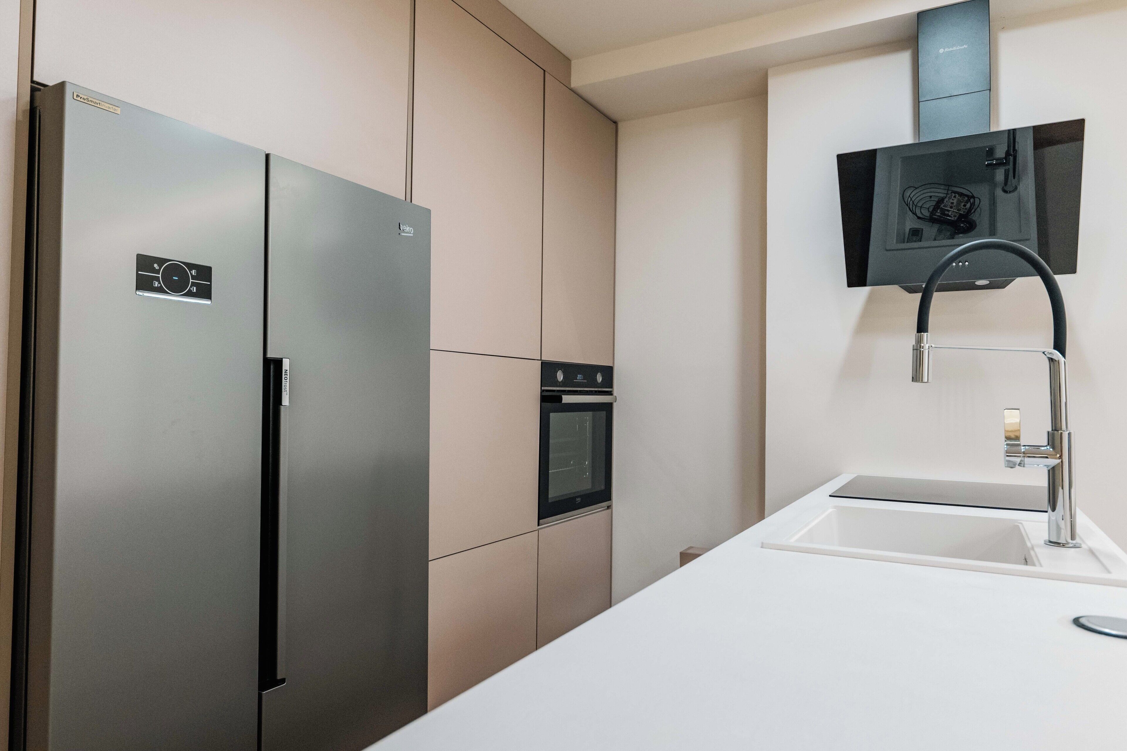A modern kitchen with a stainless steel refrigerator, built-in oven, and a sleek faucet.