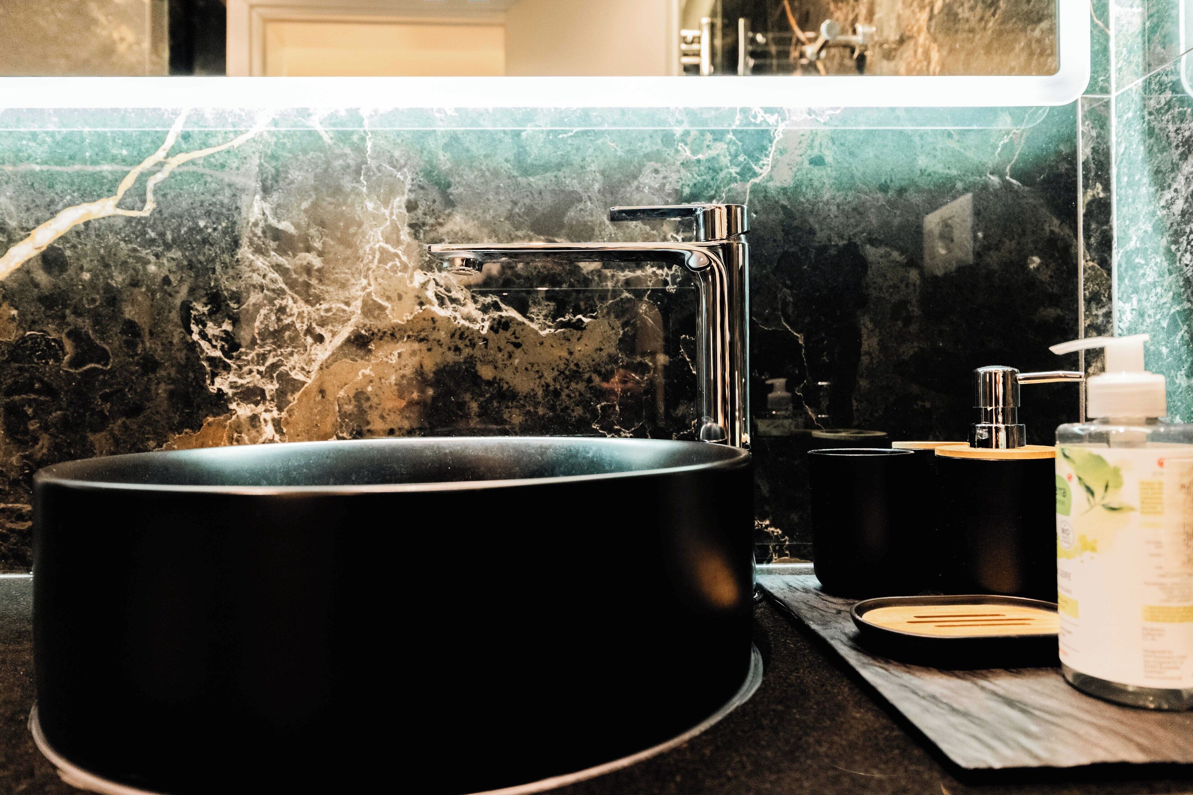 A modern bathroom with a black sink, a mirror, and a marble backsplash.