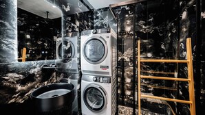 A modern laundry area with two stacked front-loading washing machines, a sink, and a wooden ladder. - Adam & Eve Apartment (Sarande)