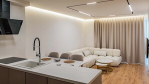 A modern kitchen with a built-in sink, a dining area with a white table and chairs, and a beige sectional sofa. - Adam & Eve Apartment (Sarande)