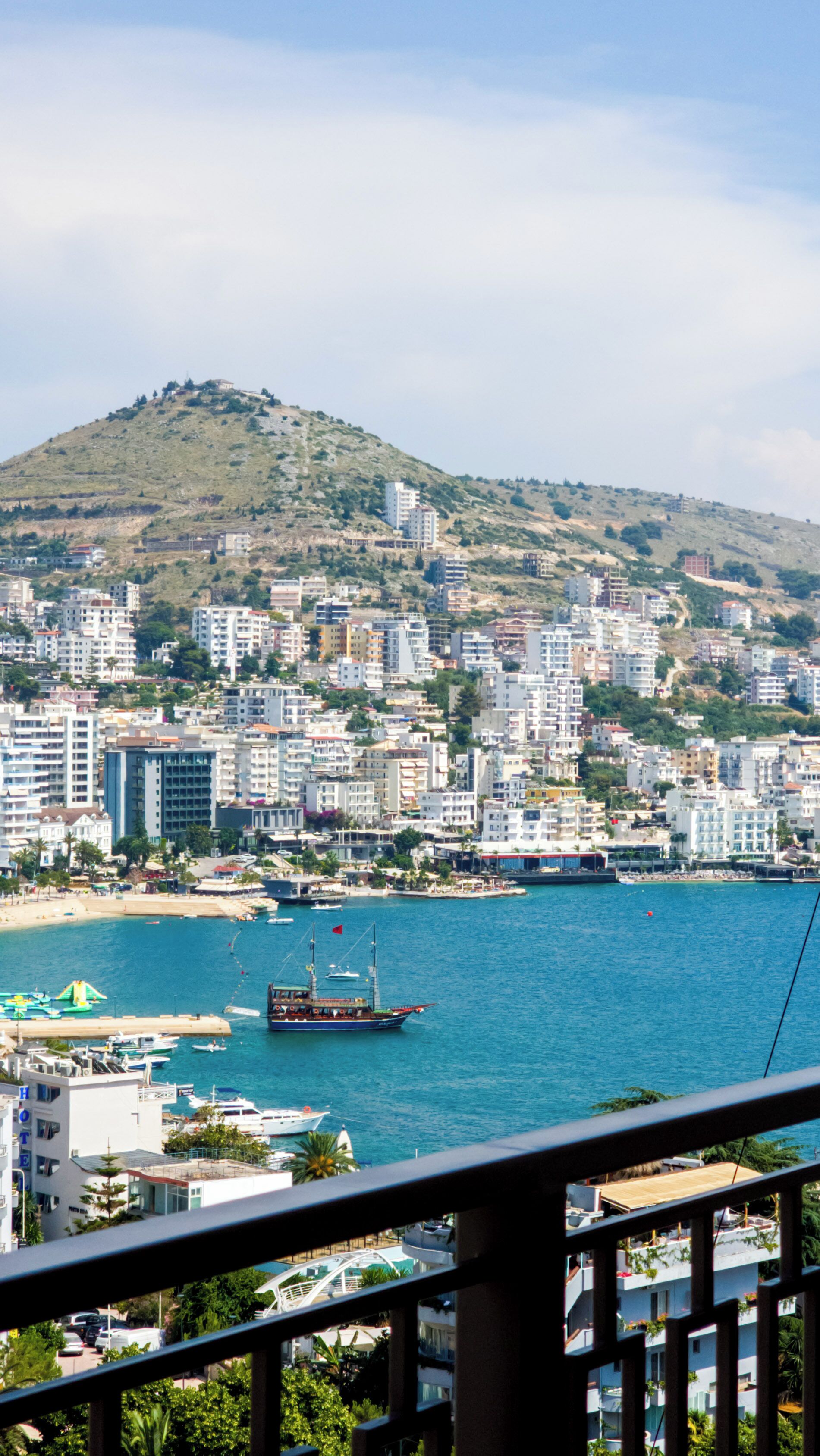 A coastal cityscape with a marina, buildings, and a hill in the background.