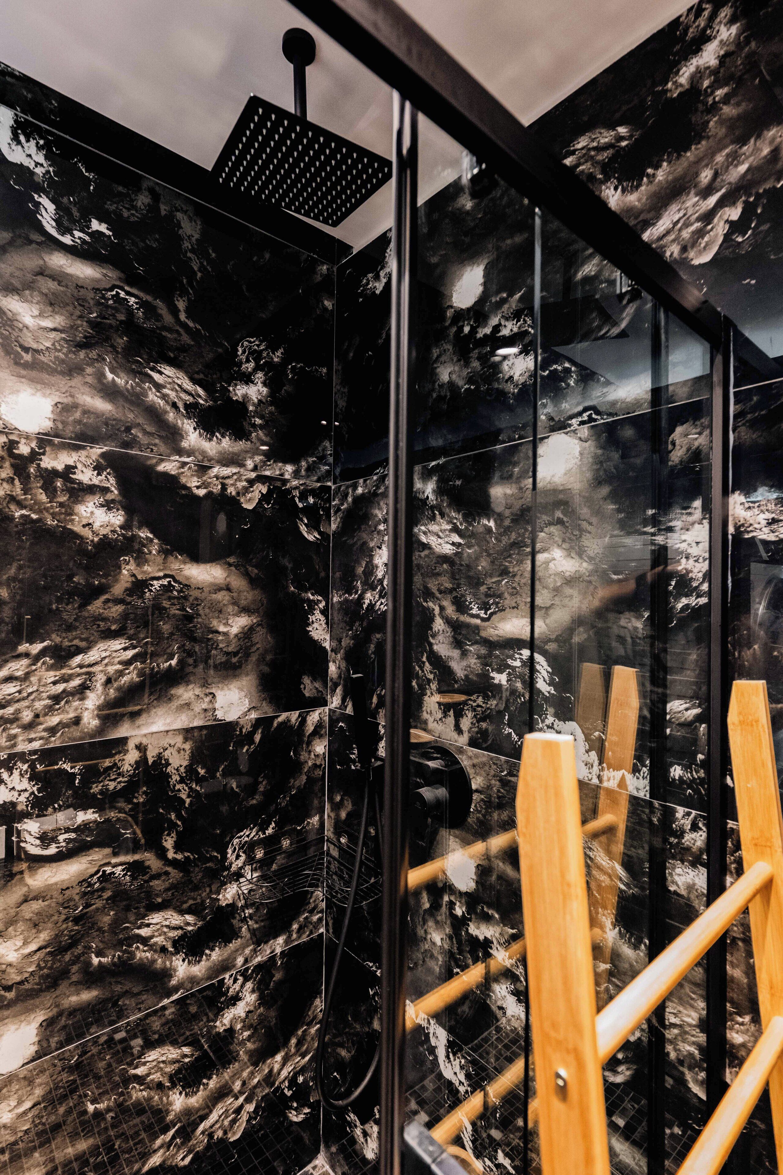 A modern bathroom with a large glass shower enclosure, a black and white marble wall, and wooden shower steps.