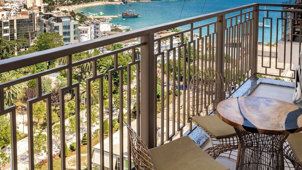 A balcony with a view of a coastal city, including buildings and a body of water. - Adam & Eve Apartment (Sarande)