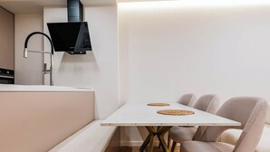A modern kitchen with a built-in stove, a black range hood, and a white dining table with four chairs. - Adam & Eve Apartment (Sarande)