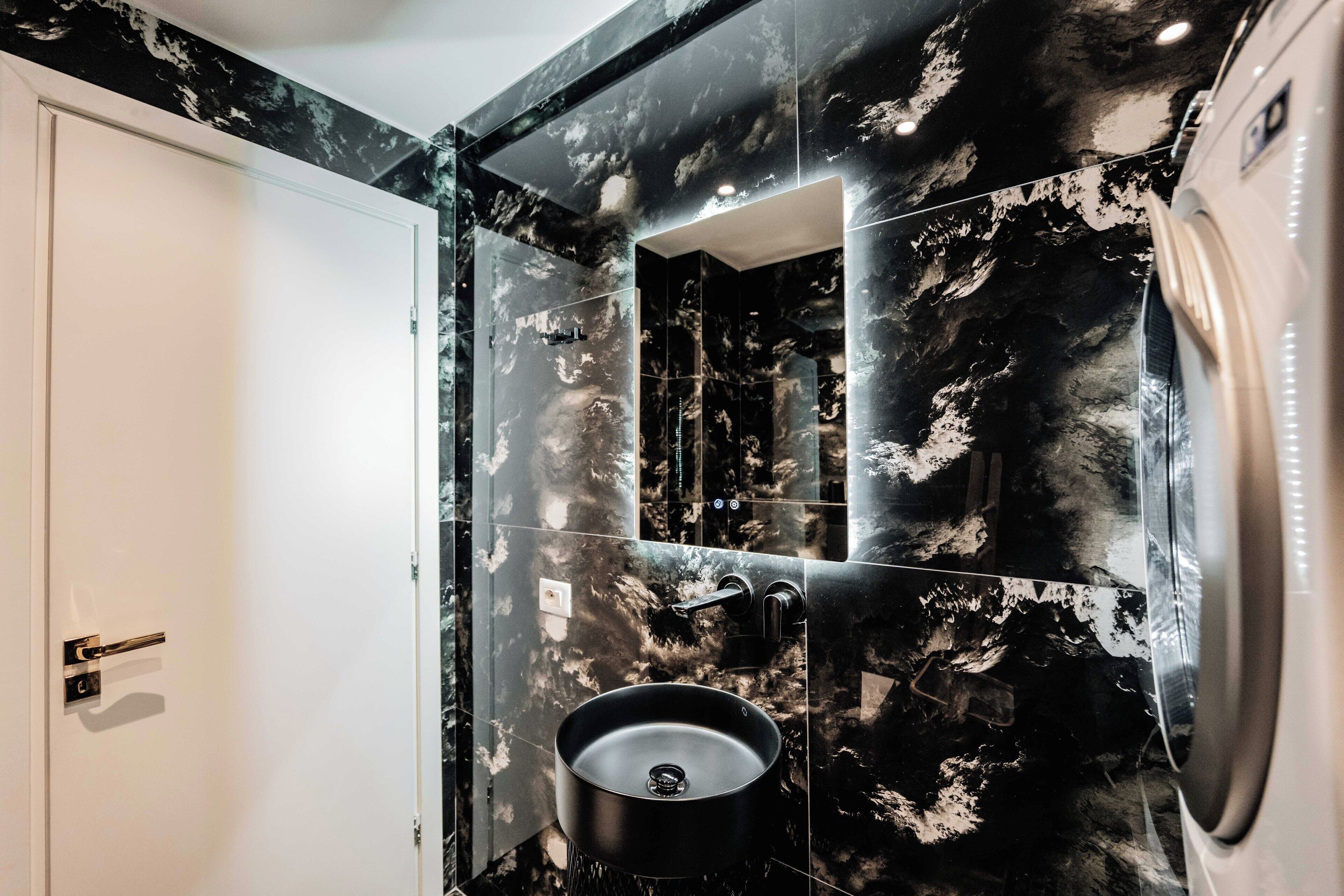 A bathroom with a black marble sink, a mirror, and a white door.