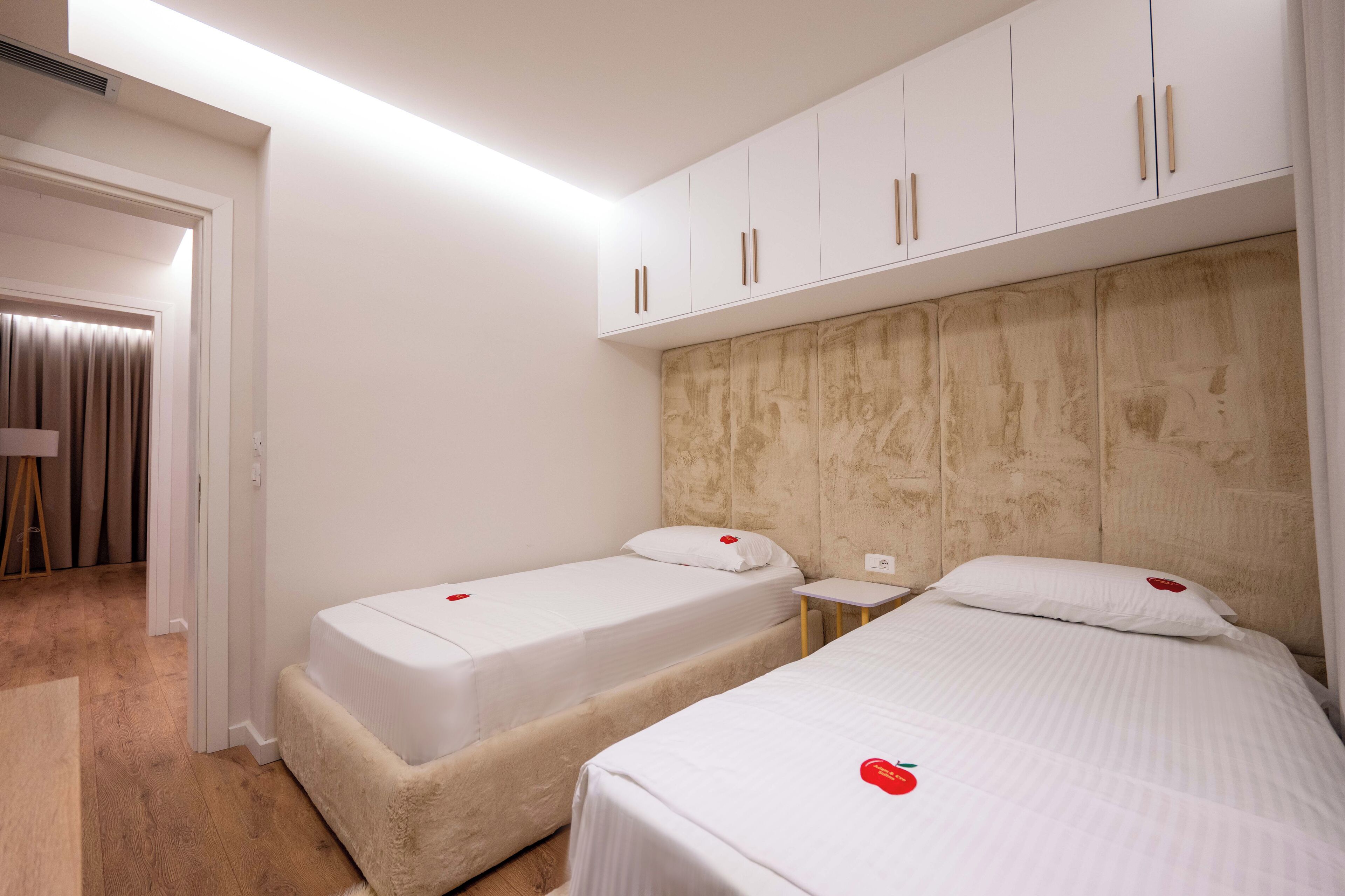 Habitación de hotel con dos camas individuales, cabecero de madera, una mesita de noche pequeña y un armario con tiradores de madera.