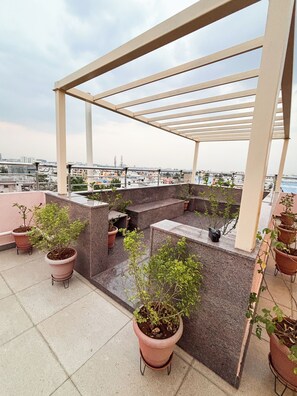 A rooftop terrace with a pergola, potted plants, and a view of the cityscape. - Visla Stay - Premium Serviced Apartment  (Bengaluru)