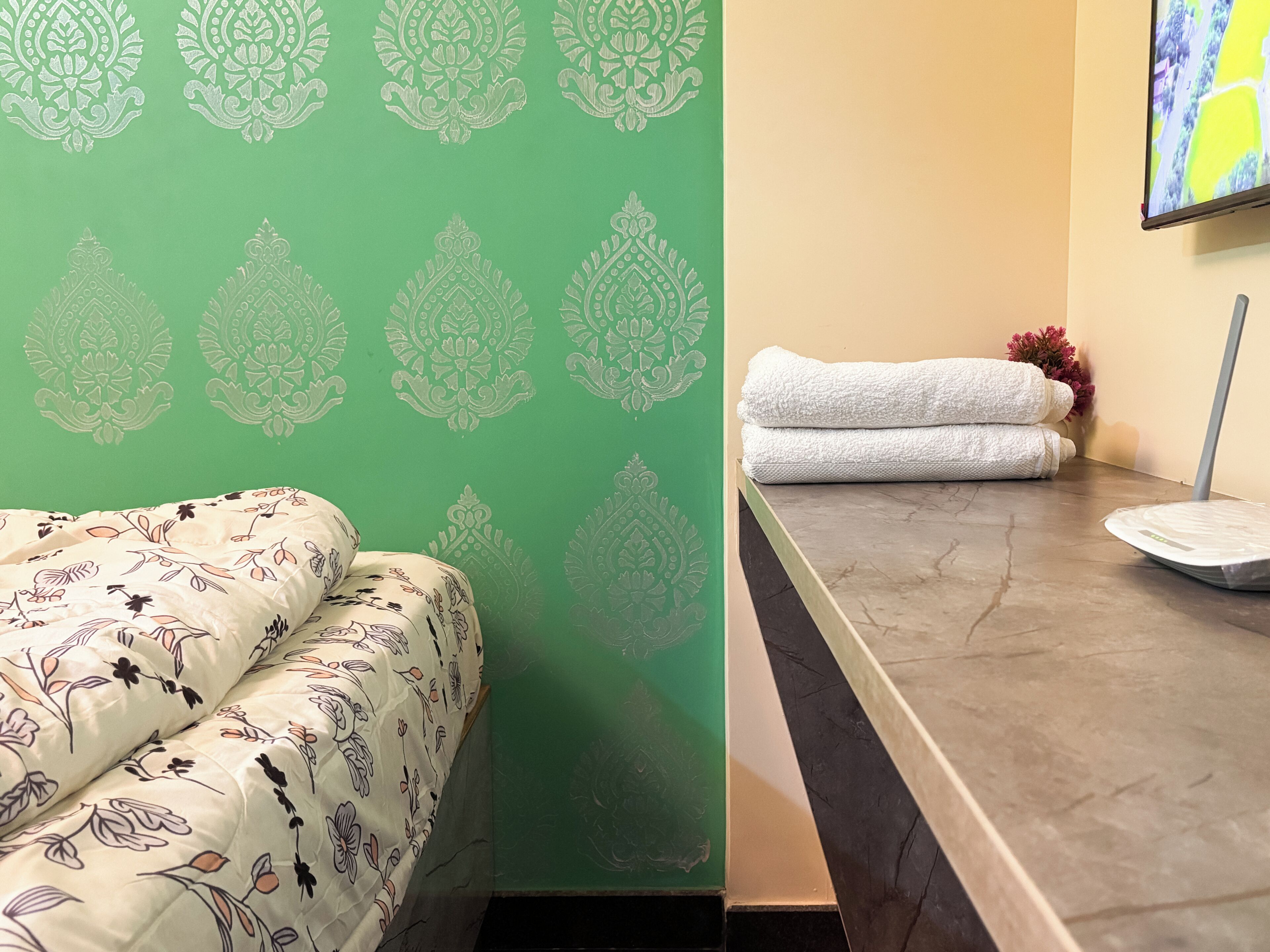 Una habitación de hotel con pared de diseño verde, una cama con ropa de cama floral, una encimera de mármol y una toalla blanca sobre la encimera.