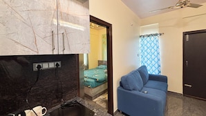 A compact living space with a kitchenette, a sofa, and a ceiling fan. - Visla Stay - Premium Serviced Apartment  (Bengaluru)