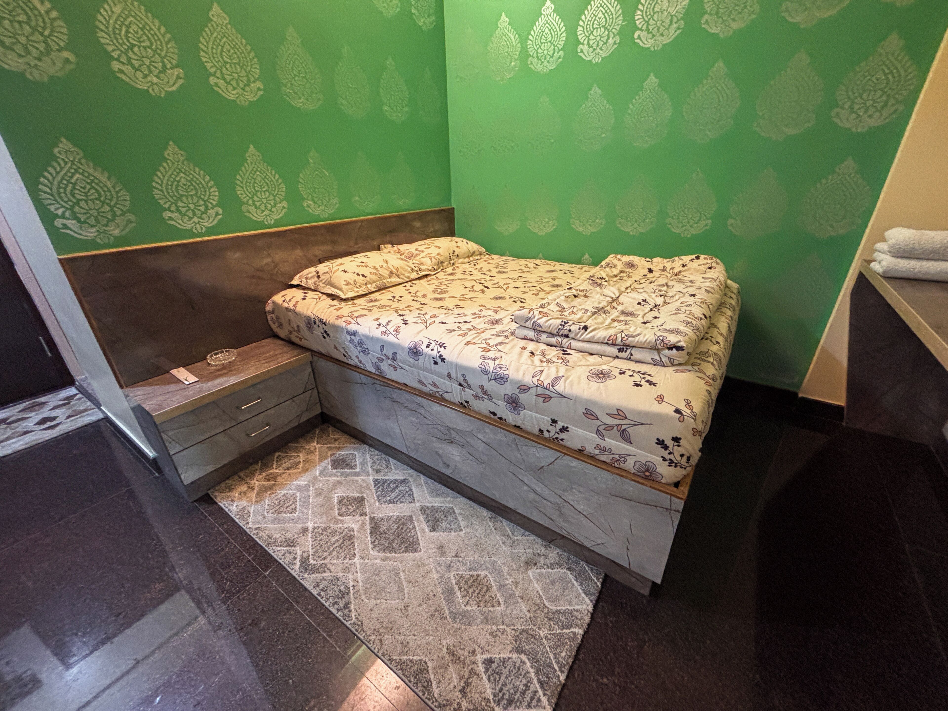 Una habitación pequeña y funcional con una cama, una mesita de noche y una pequeña mesa.