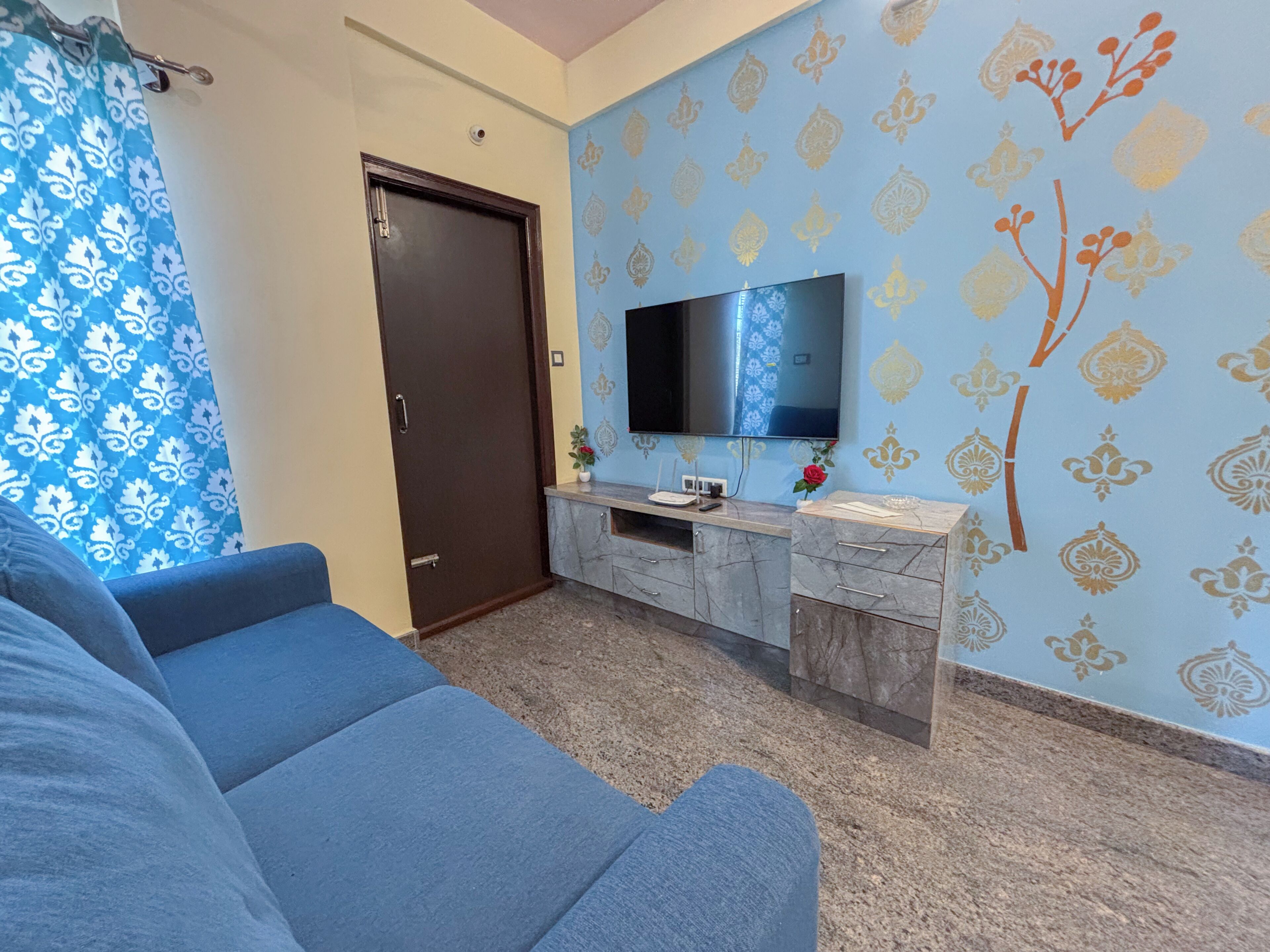 Un salon avec un canapé, un téléviseur fixé au mur, une porte et un mur décoré d’un motif.