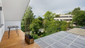 A balcony with a wooden floor, a small table, a vertical garden, and a view of a residential area with trees and buildings.