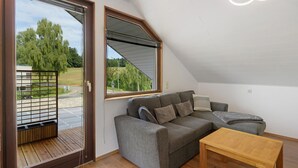 A modern living room with a grey sofa, a wooden coffee table, and a large window with a view of greenery.
