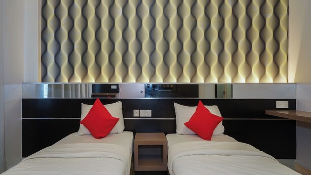 Habitación de hotel con dos camas, un panel de pared moderno, una mesita de noche de madera y un estante empotrado.