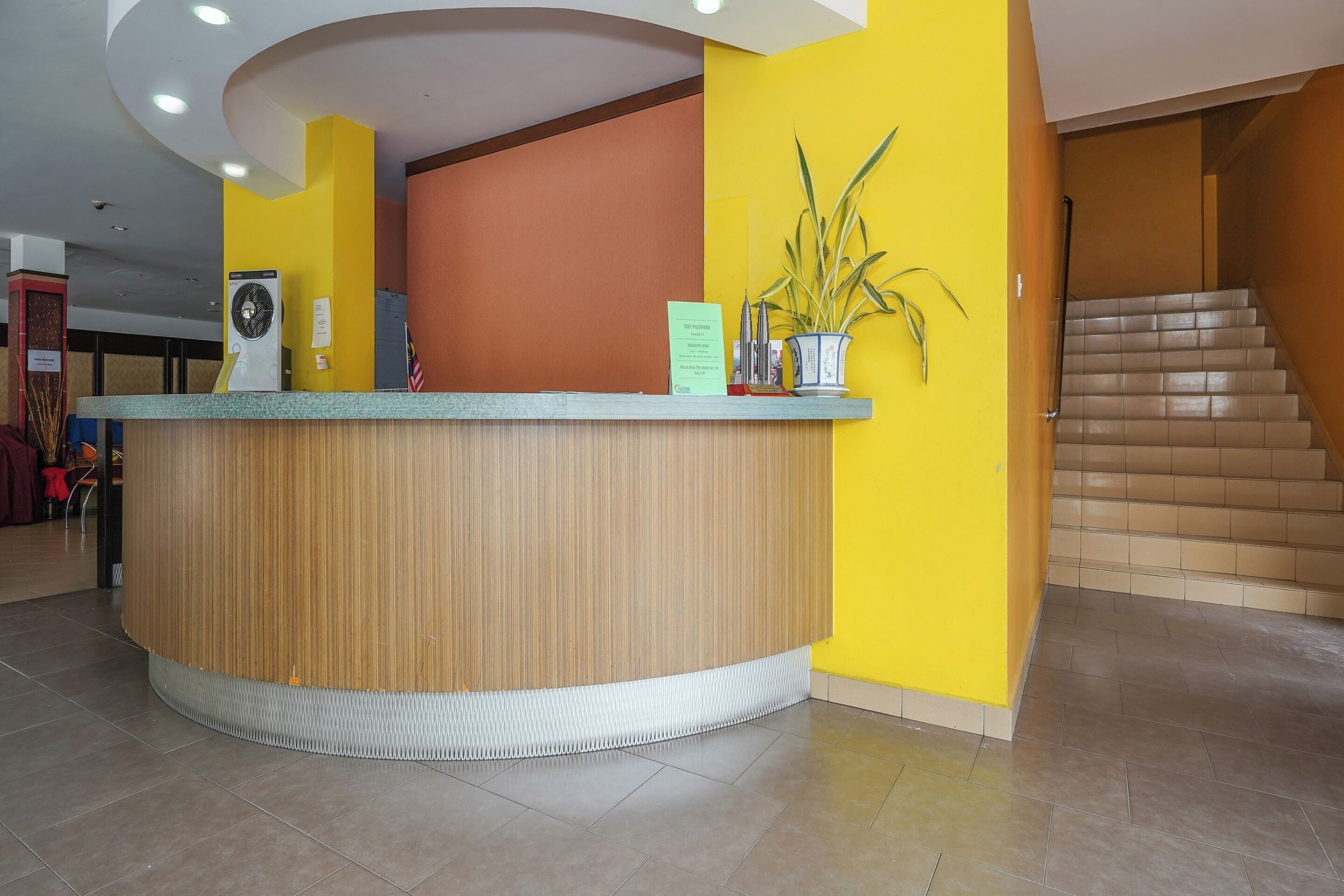 A reception desk with a wooden finish, a potted plant, and a sign indicating a waiting area.