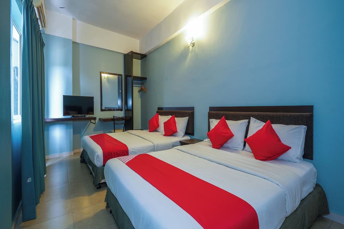 A hotel room with two beds, each with red and white bedding, a desk with a chair, a mirror, and a TV.