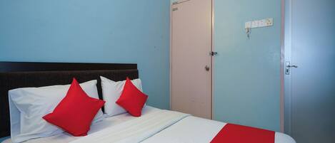 A neatly made bed with white and red bedding, a closed door, and a wall-mounted electrical outlet.