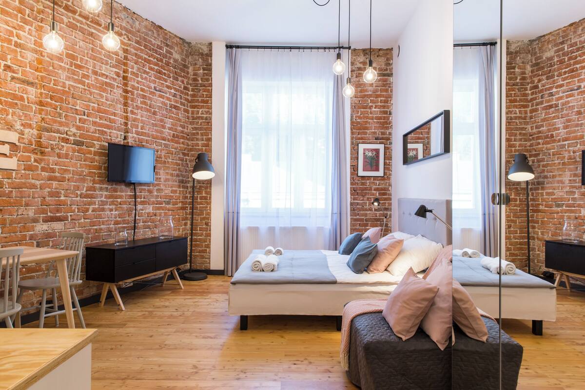 Un dormitorio moderno con pared de ladrillo, una cama grande con almohadas, un escritorio y una silla.