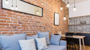 A modern living space with a brick wall, a sofa with patterned cushions, a dining area with a table and chairs, and pendant lighting. - 19Rooms (Kraków)