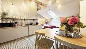 A modern kitchen with a patterned backsplash, a dining area with a table and chairs, and a bedroom with a bed and a window. - 19Rooms (Kraków)