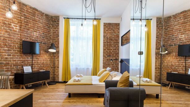 A modern room with a brick wall, a bed with yellow curtains, a desk, and a chair. - 19Rooms (Kraków)