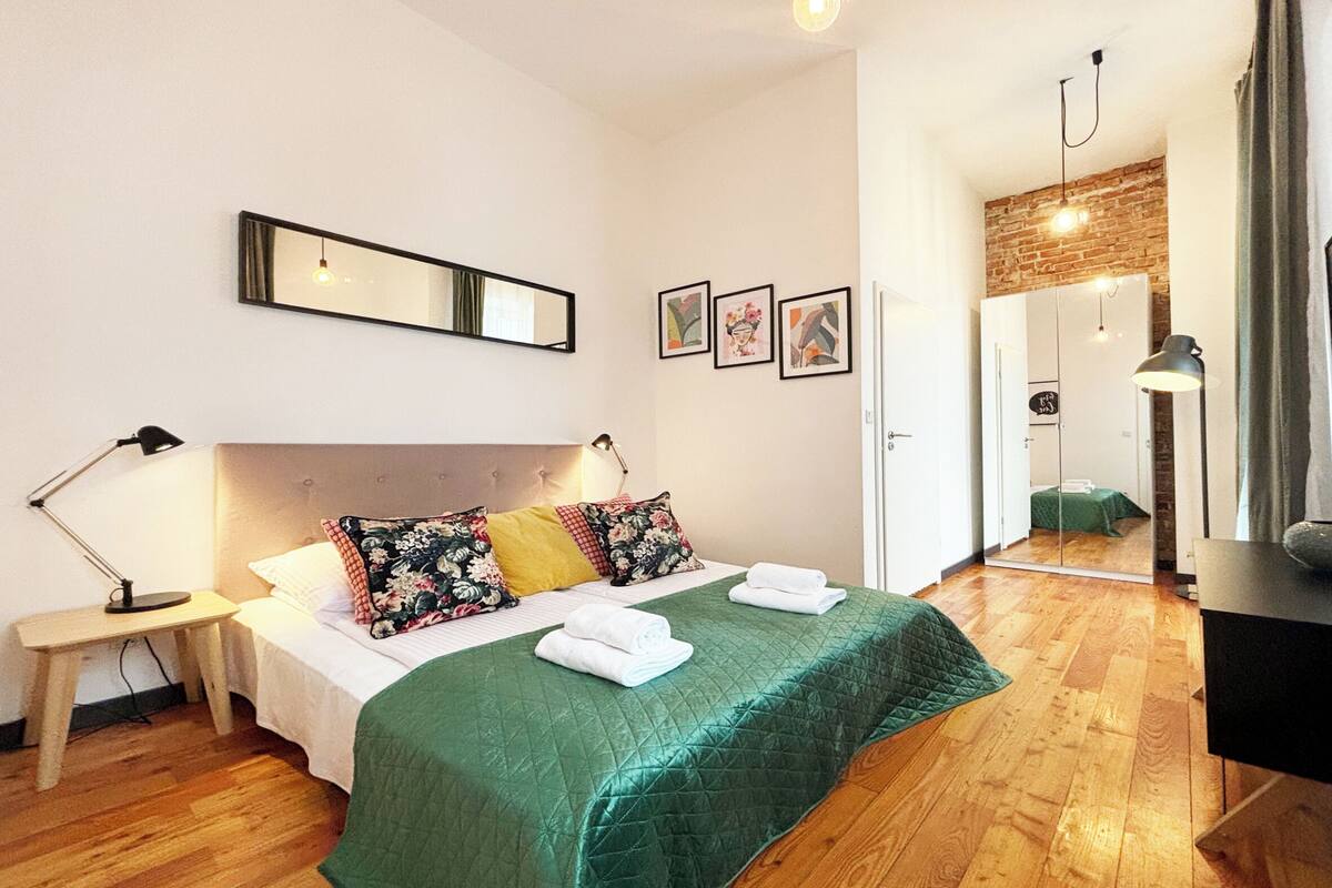 Una habitación de hotel con cama, mesita de noche, espejo y cuadros en la pared.