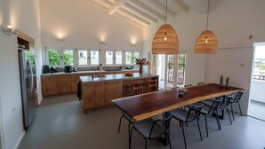 Een ruime keuken met een groot schiereiland, houten keukenkastjes en een eethoek met een lange tafel en stoelen.