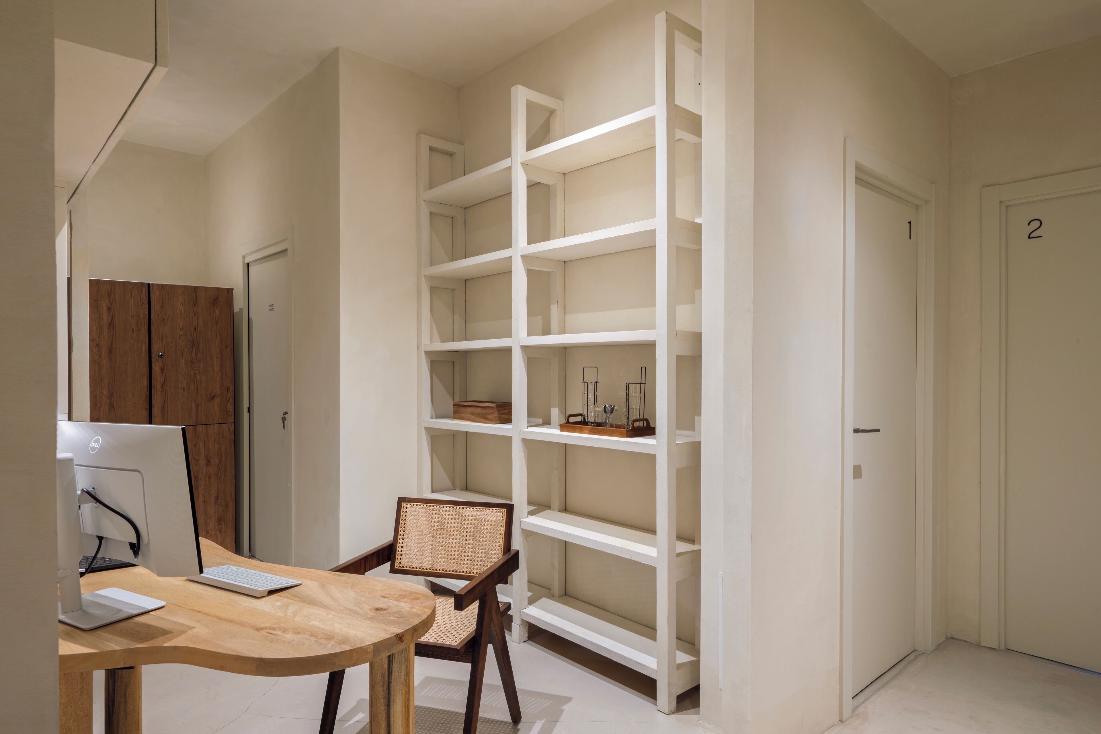 Una habitación con escritorio, silla, computadora y una estantería blanca.