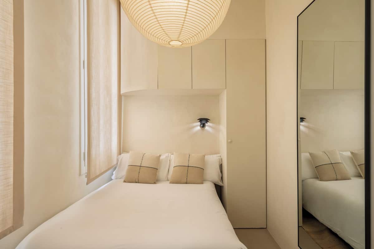 A bedroom with a large bed, a bedside lamp, and a mirror on the wall.