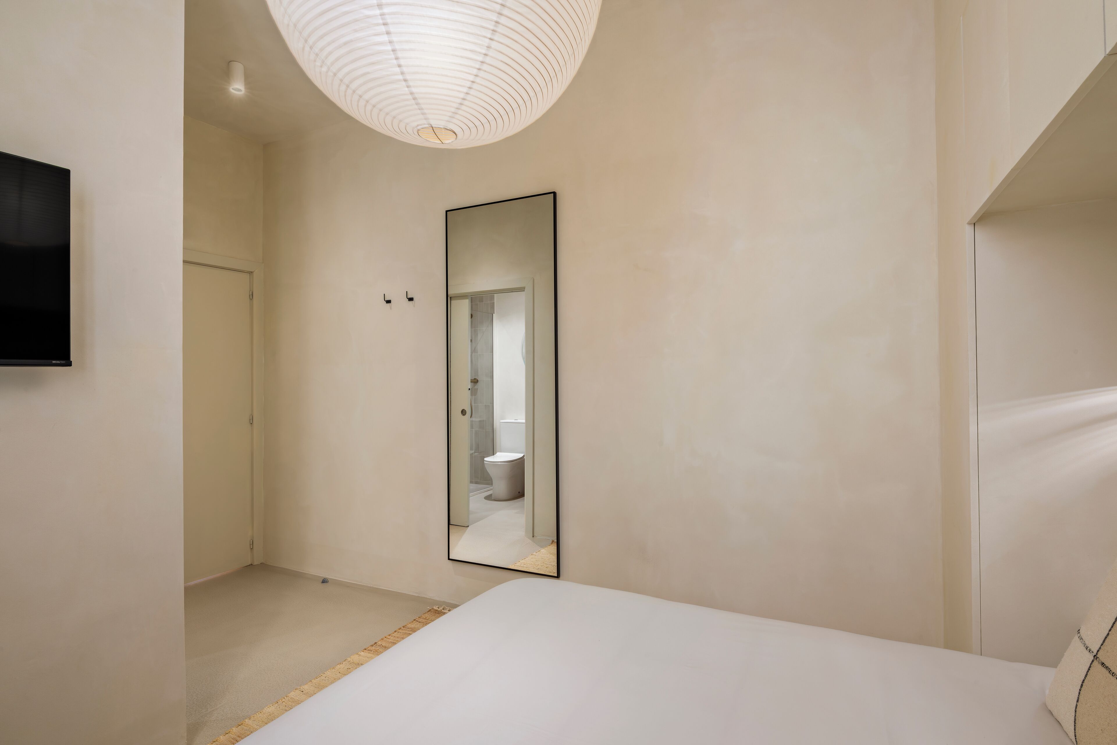 A modern bedroom with a large mirror, a flat-screen TV, and a minimalist design.