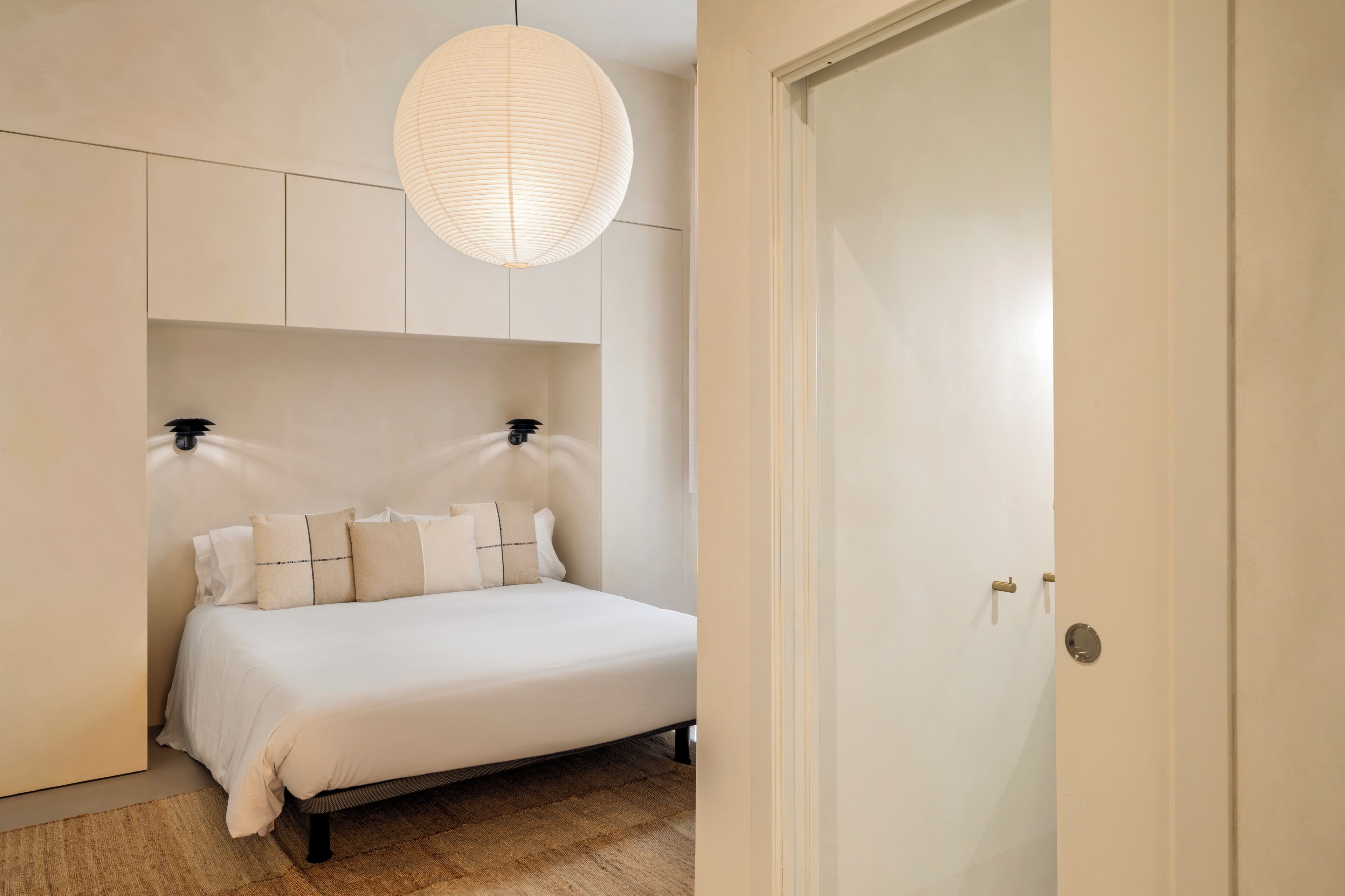 Une chambre à coucher avec un lit, un luminaire suspendu et une porte.