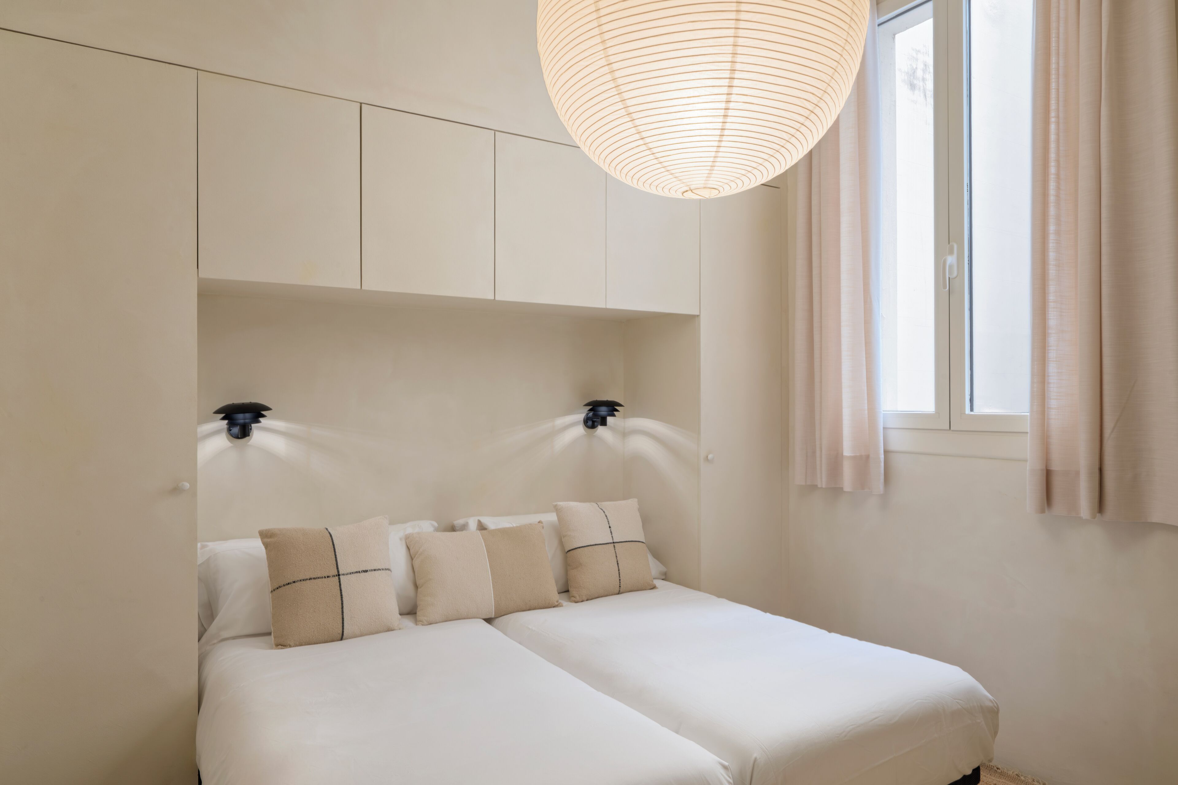 A bedroom with two beds, a ceiling light fixture, and a window with curtains.