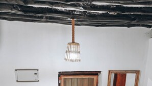 A room with a wooden window, a wooden door, a small table with a pot, a hanging light fixture, and a staircase railing.